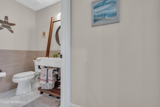 bathroom featuring wainscoting, tile walls, and toilet