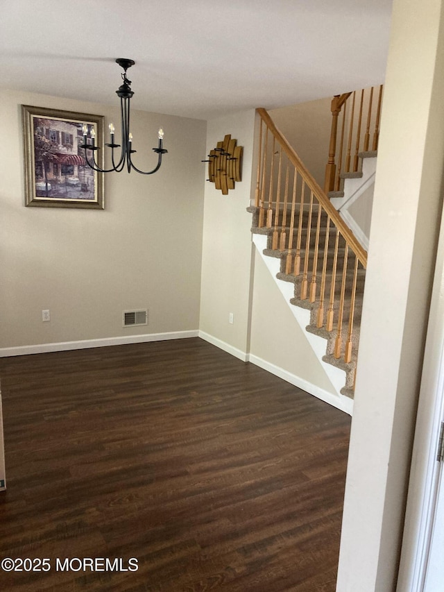 spare room with a chandelier, wood finished floors, visible vents, baseboards, and stairway