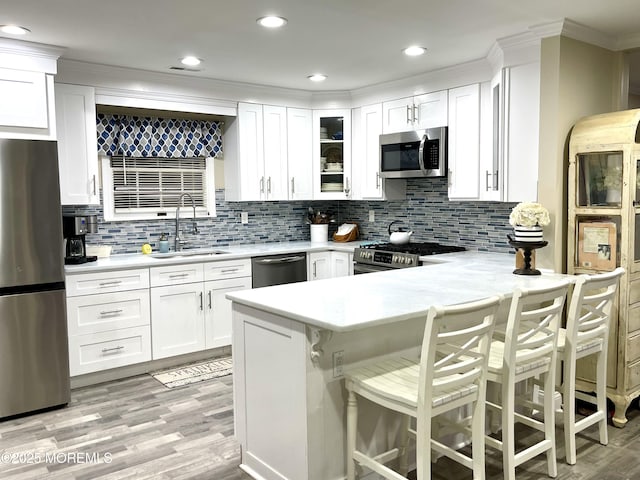 kitchen with light countertops, appliances with stainless steel finishes, a peninsula, white cabinets, and a sink