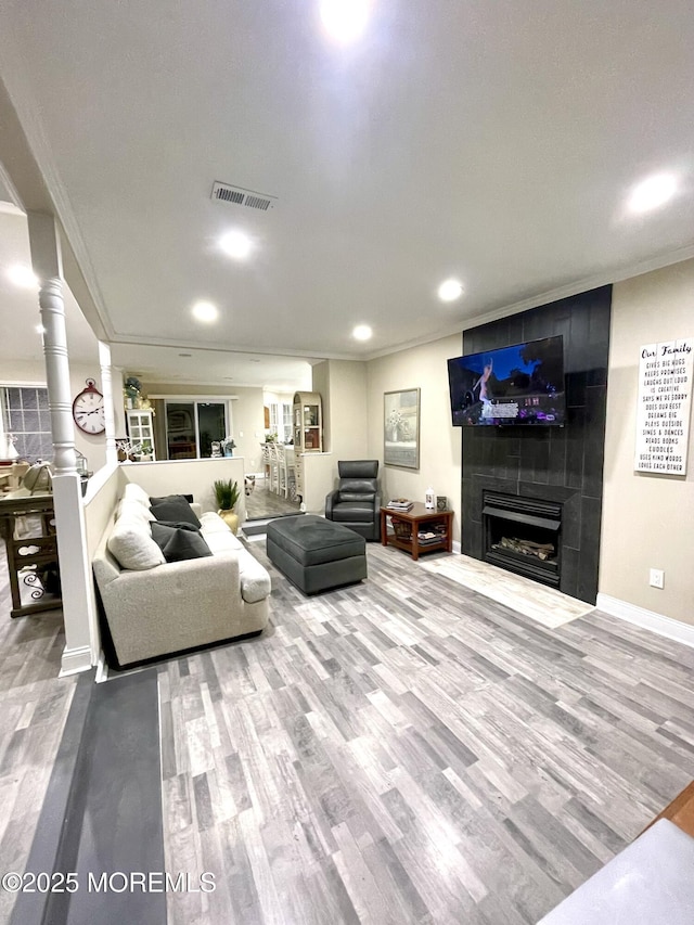 living room with wood finished floors, visible vents, decorative columns, a tiled fireplace, and crown molding