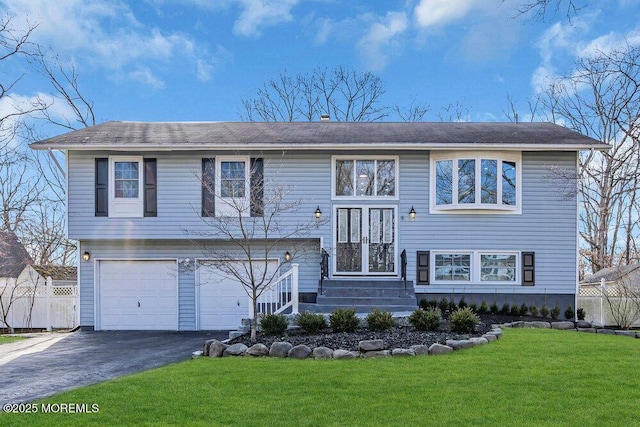 bi-level home with driveway, a garage, fence, and a front yard