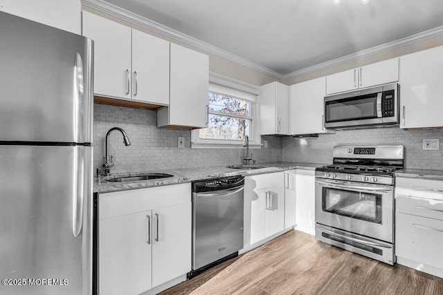 kitchen with ornamental molding, appliances with stainless steel finishes, a sink, and light stone counters