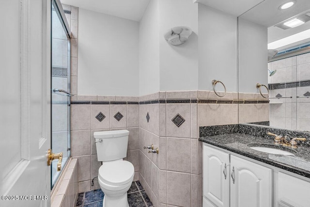 full bath featuring toilet, tile patterned flooring, tiled shower / bath, vanity, and tile walls