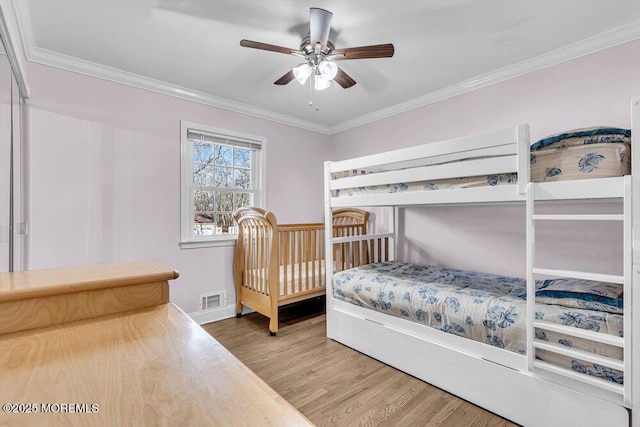 bedroom featuring a ceiling fan, visible vents, crown molding, and wood finished floors