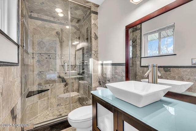 bathroom featuring toilet, vanity, tile walls, wainscoting, and a shower stall