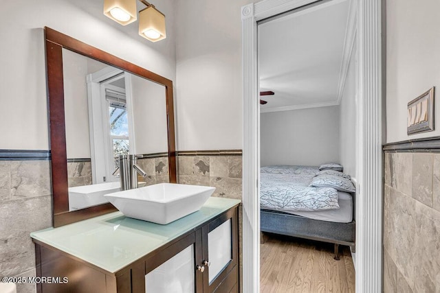 ensuite bathroom with tile walls, ornamental molding, wainscoting, vanity, and ensuite bath