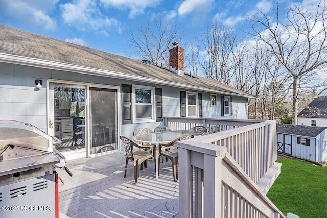 deck with outdoor dining space, a shed, a yard, and an outbuilding