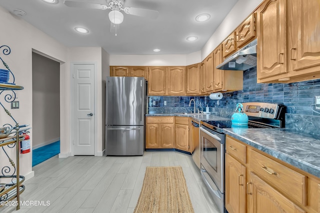 kitchen featuring light wood-style floors, dark countertops, appliances with stainless steel finishes, under cabinet range hood, and a sink