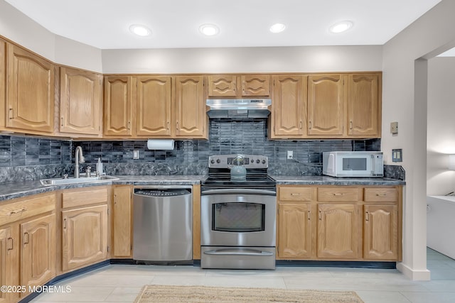 kitchen featuring tasteful backsplash, dark countertops, appliances with stainless steel finishes, under cabinet range hood, and a sink