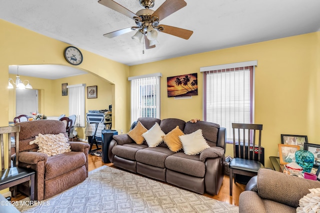 living area with ceiling fan with notable chandelier, arched walkways, a healthy amount of sunlight, and wood finished floors