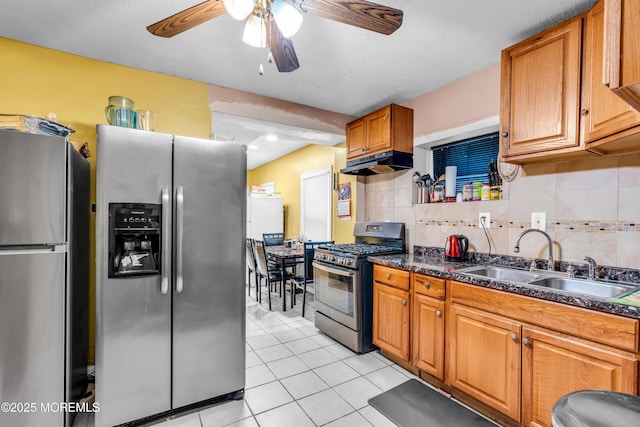 kitchen with light tile patterned floors, under cabinet range hood, a sink, appliances with stainless steel finishes, and dark countertops