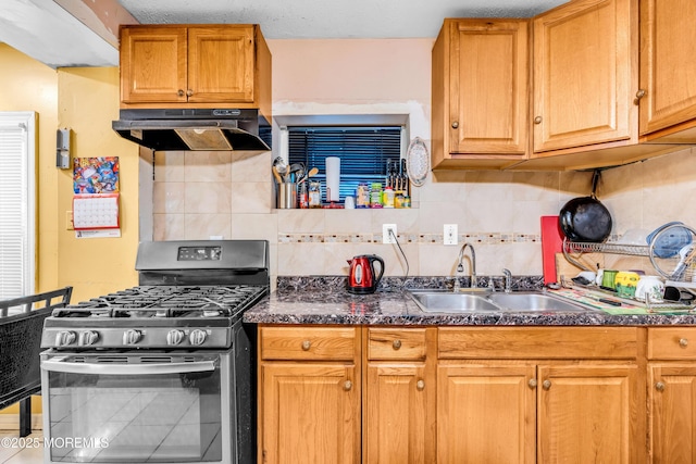 kitchen featuring dark countertops, stainless steel range with gas stovetop, a sink, and under cabinet range hood