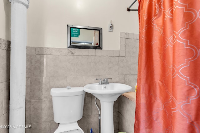 bathroom with a wainscoted wall, curtained shower, toilet, and tile walls