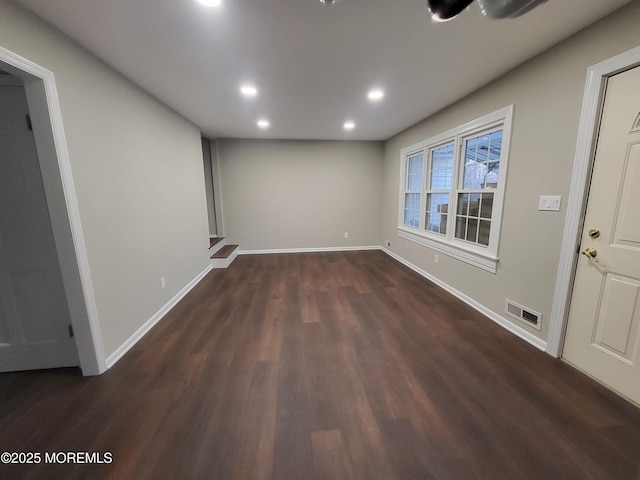 empty room with dark wood-style floors, recessed lighting, visible vents, and baseboards