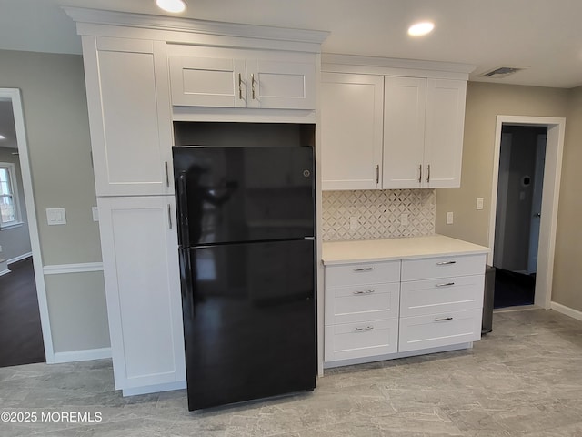 kitchen with tasteful backsplash, visible vents, white cabinets, freestanding refrigerator, and light countertops