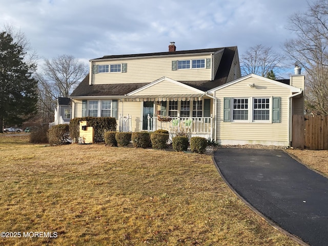 traditional-style home with covered porch, a chimney, fence, and a front yard