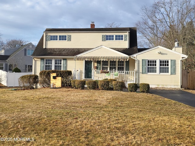 traditional home featuring a front yard, covered porch, fence, and a chimney