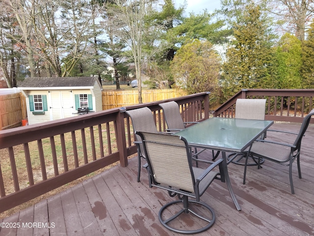 wooden terrace with a shed, outdoor dining area, an outdoor structure, and fence