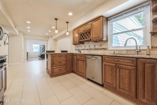 kitchen featuring tasteful backsplash, light stone counters, brown cabinets, stainless steel dishwasher, and a sink