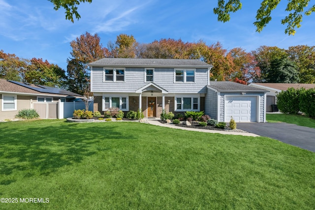 colonial house featuring aphalt driveway, brick siding, an attached garage, fence, and a front lawn