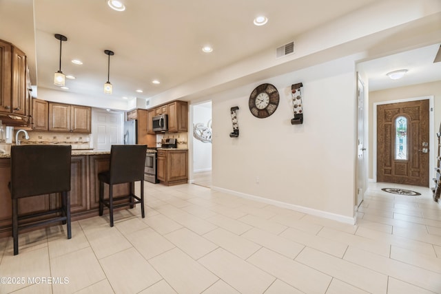 kitchen with visible vents, a breakfast bar area, brown cabinets, stainless steel appliances, and backsplash