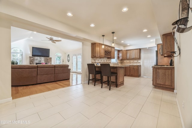 kitchen with a peninsula, open floor plan, backsplash, brown cabinetry, and a kitchen bar