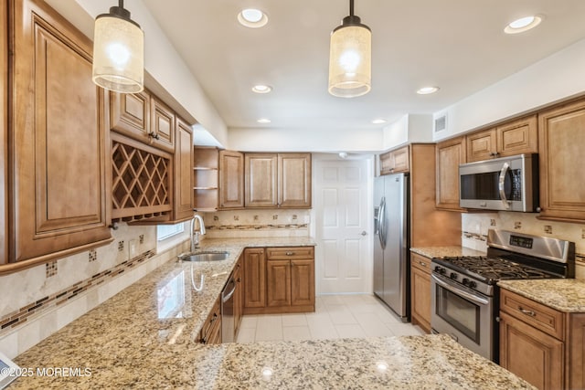 kitchen featuring appliances with stainless steel finishes, brown cabinets, a sink, and light stone counters