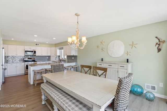 dining room with light wood finished floors, visible vents, recessed lighting, and a notable chandelier