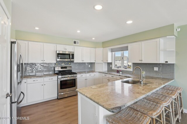 kitchen with visible vents, a sink, open shelves, stainless steel appliances, and a peninsula