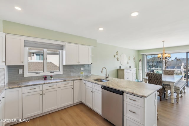 kitchen featuring light wood finished floors, white cabinetry, a peninsula, a sink, and dishwasher