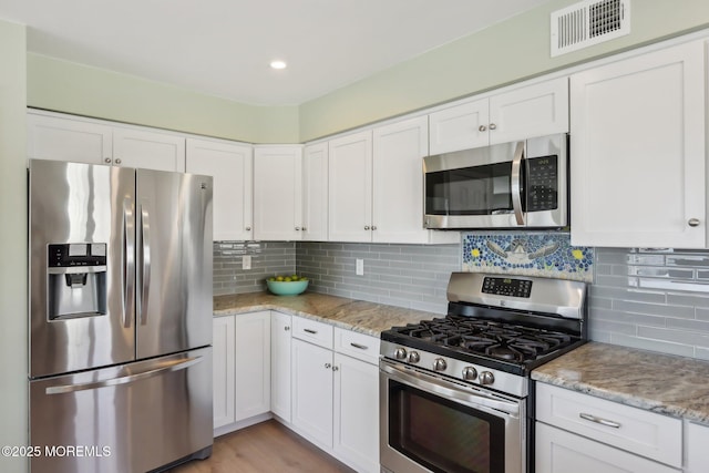 kitchen featuring stainless steel appliances, tasteful backsplash, visible vents, and white cabinets