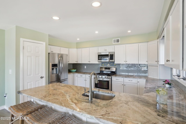 kitchen featuring visible vents, backsplash, stainless steel appliances, a peninsula, and light stone countertops