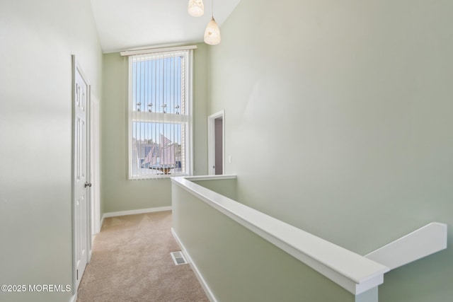 hall with baseboards, light carpet, visible vents, and an upstairs landing