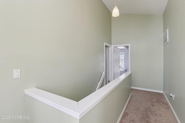 hallway with visible vents, an upstairs landing, high vaulted ceiling, carpet, and baseboards