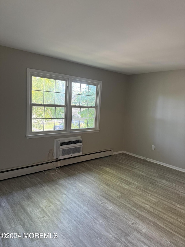 spare room with a baseboard heating unit, a wall mounted AC, wood finished floors, and baseboards