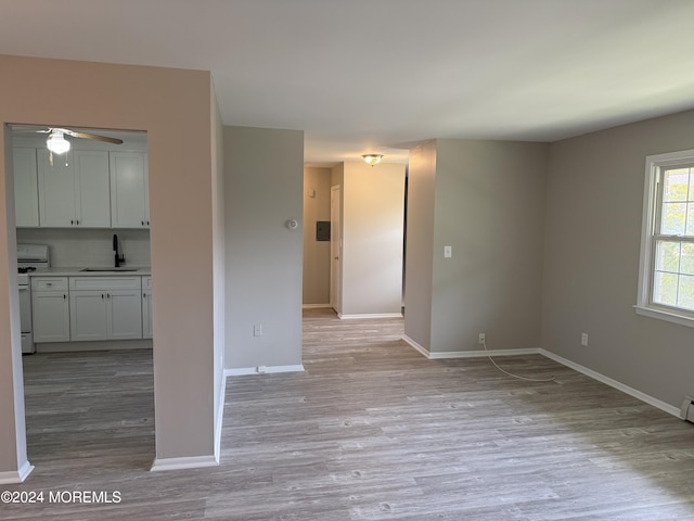 spare room featuring light wood-style floors, a ceiling fan, baseboards, and a sink