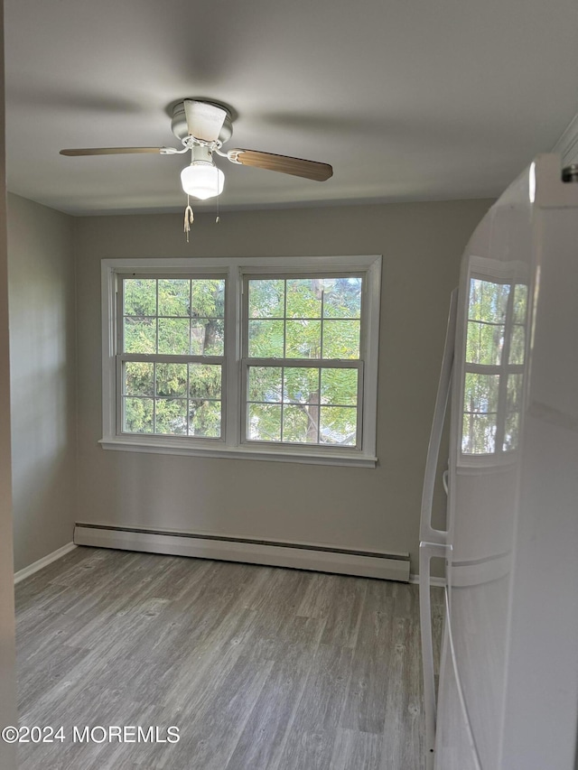 spare room featuring arched walkways, baseboard heating, and wood finished floors