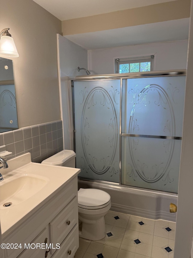 bathroom with toilet, tile patterned flooring, combined bath / shower with glass door, vanity, and tile walls