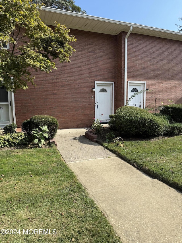 view of exterior entry with a yard and brick siding