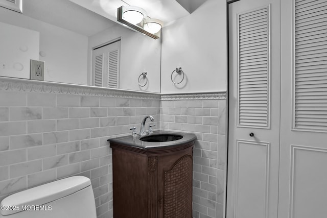 bathroom with vanity, a wainscoted wall, a closet, tile walls, and toilet