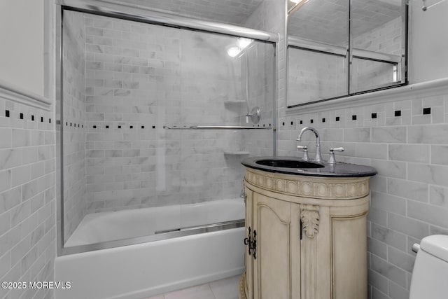 bathroom featuring tile patterned floors, combined bath / shower with glass door, tile walls, and vanity