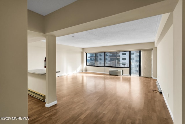 empty room with wood finished floors, baseboards, baseboard heating, and a textured ceiling