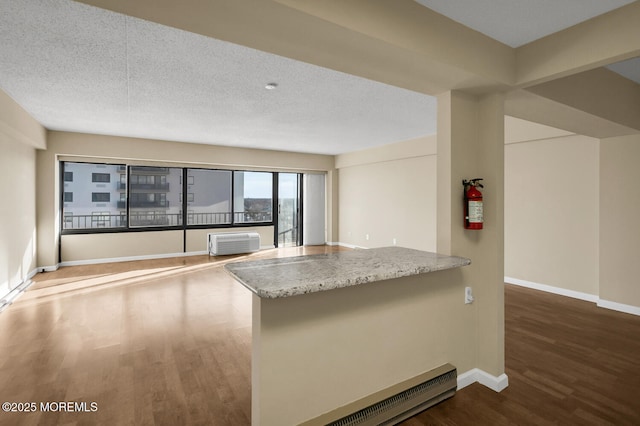 kitchen featuring baseboards, light stone countertops, wood finished floors, a textured ceiling, and a wall mounted AC