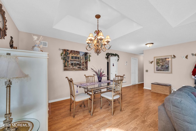 dining area featuring light wood-type flooring, a tray ceiling, visible vents, and baseboards