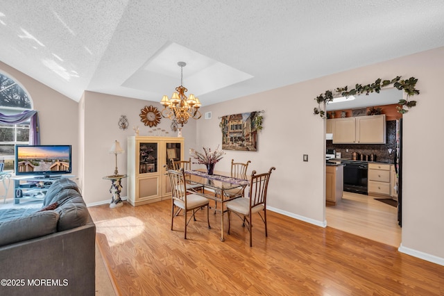 dining area featuring light wood-type flooring, baseboards, a raised ceiling, and a textured ceiling