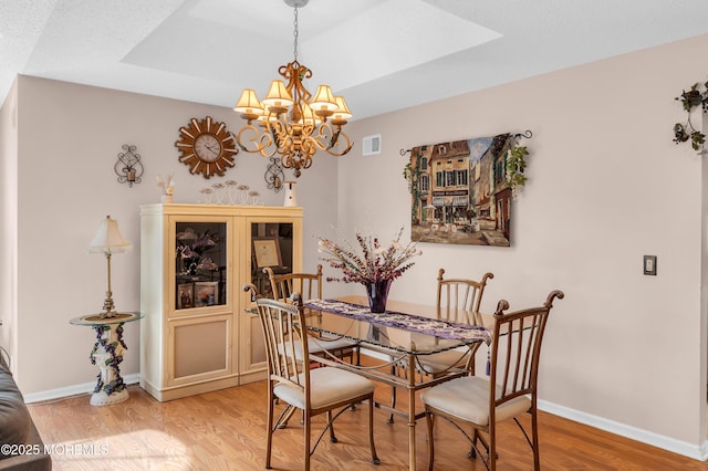 dining area with light wood-type flooring, baseboards, visible vents, and a tray ceiling