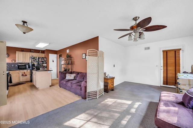 living room with ceiling fan, light wood finished floors, and visible vents