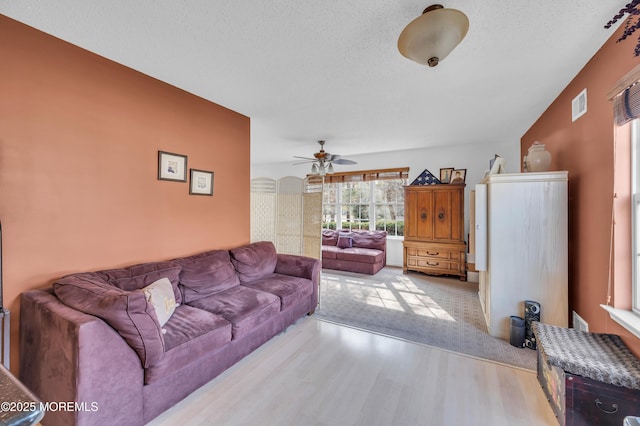 living room with a ceiling fan, a textured ceiling, visible vents, and wood finished floors