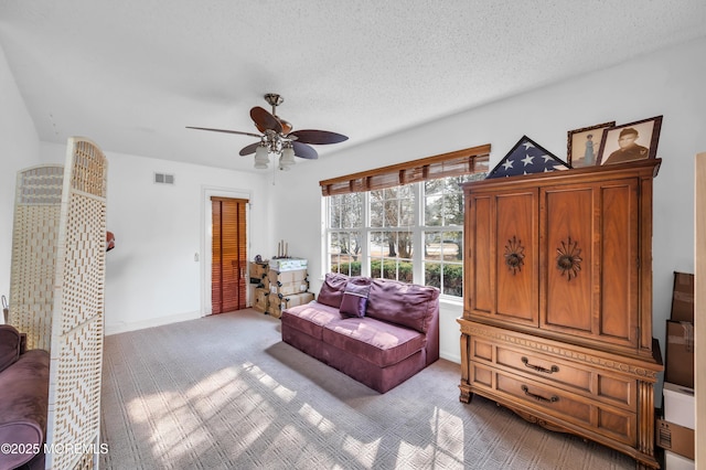 living area featuring a textured ceiling, visible vents, baseboards, a ceiling fan, and carpet