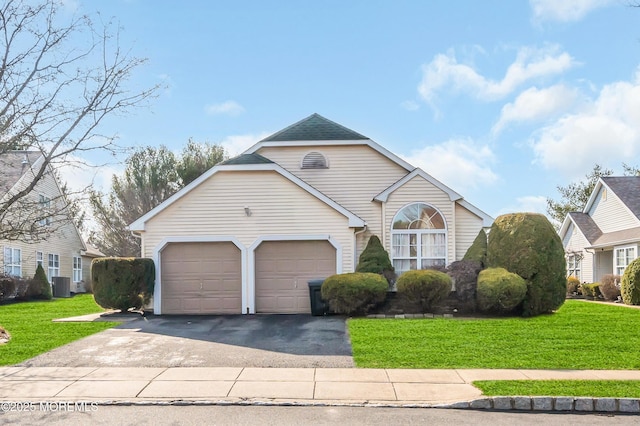 traditional-style home featuring an attached garage, central AC, a shingled roof, driveway, and a front yard